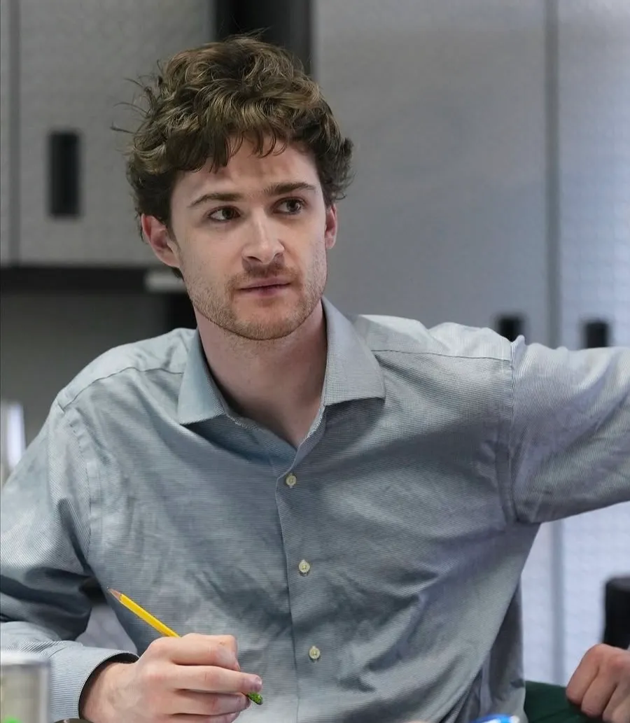 Andrew Hardigg in a grey button-down shirt holding a pencil, glancing off camera