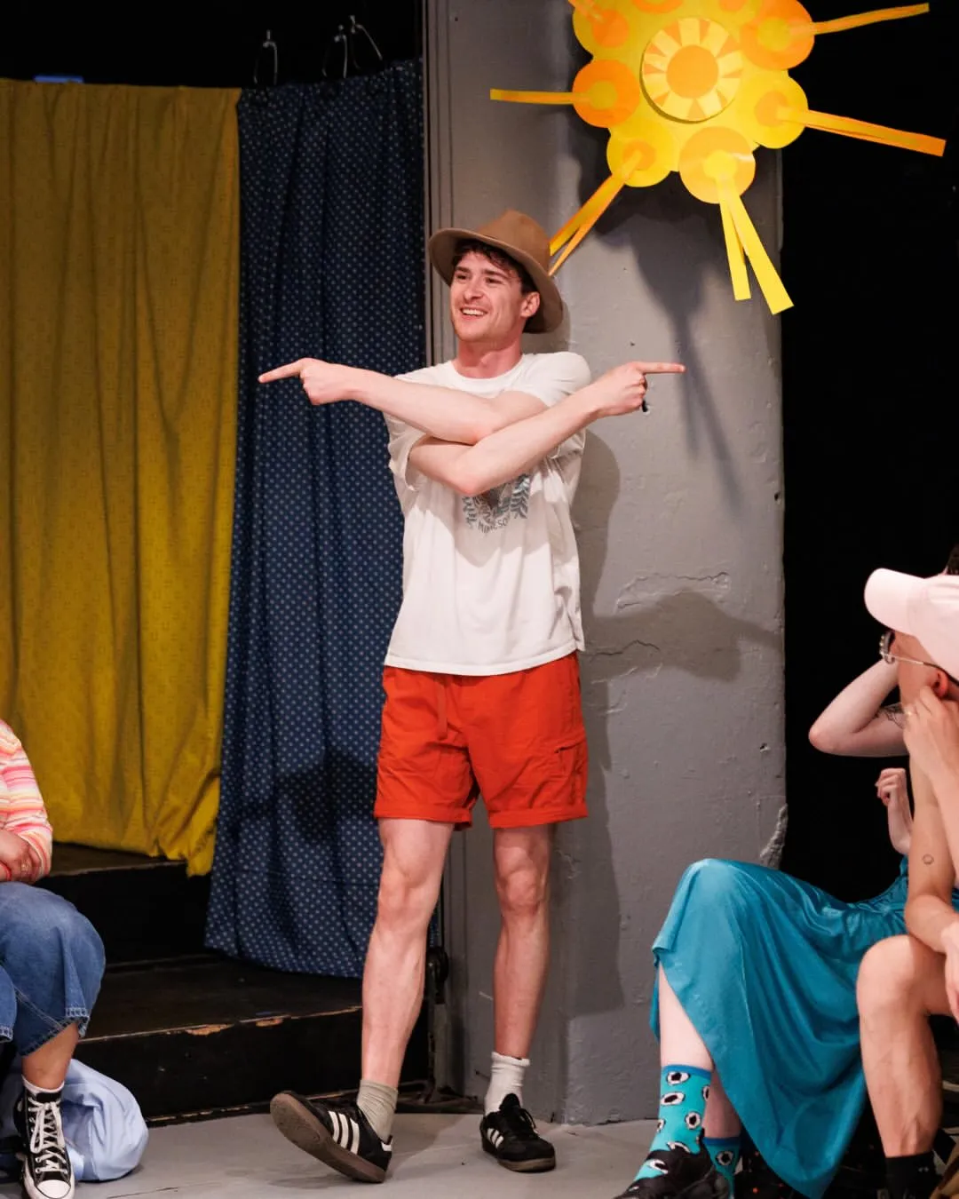 Andrew Hardigg in a wide-brimmed hat pointing in both directions, grinning, mid-scene