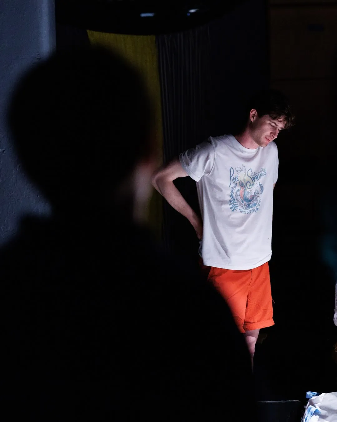 Andrew Hardigg standing in the wings with a hand on his hip, watching the stage